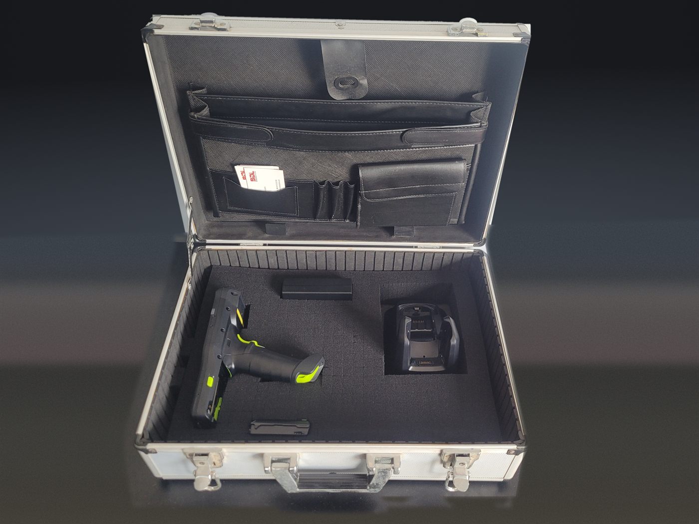An aluminium flight case open on a bench, foam cut to hold a Zebra MC3400
                    gun-grip terminal, its power supply and a charging cradle, with a Barcode
                    Datalink card in the lid pocket.